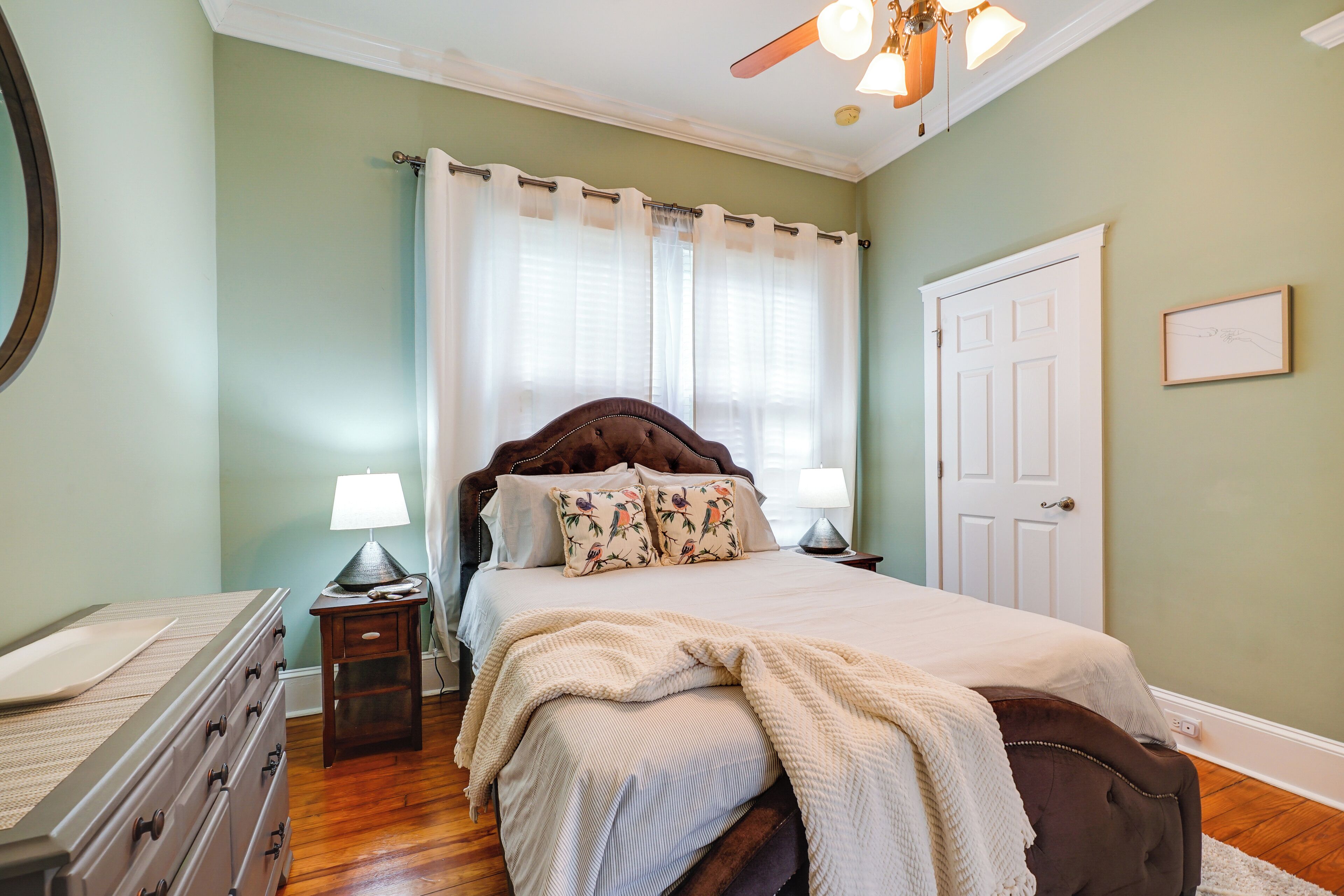 Un dormitorio con cama, cómoda, mesita de noche, lámpara, ventilador de techo y puerta.