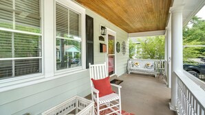 Ein überdachter Balkon mit weißen Geländern, einem roten Teppich mit Muster und einem weißen Stuhl mit roter Sitzkissen.
