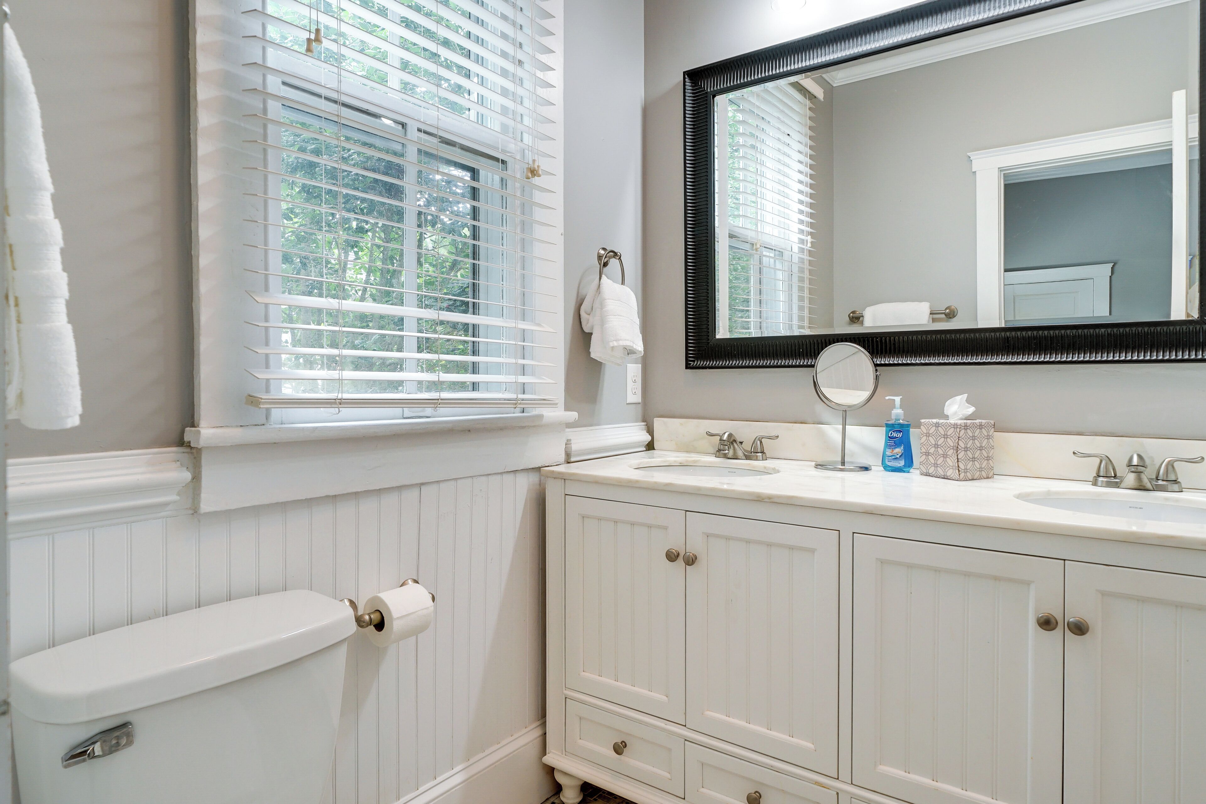 A bathroom with a toilet, a sink with a mirror, and a window with blinds.