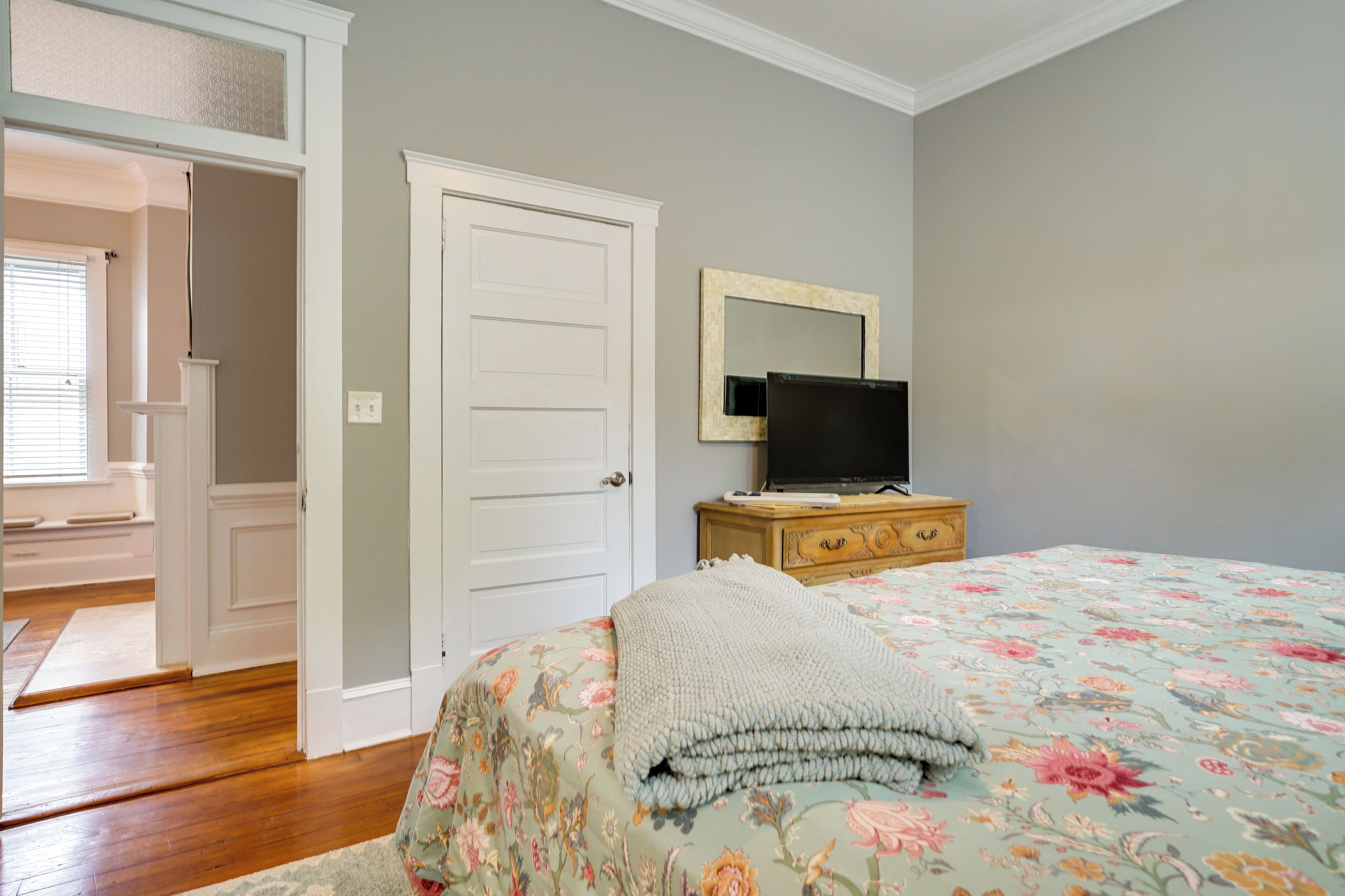 A bedroom with a bed, a television on a dresser, and a door leading to another room.