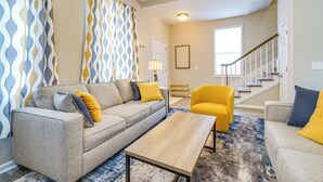 Sala de estar con sofá, mesa de centro y sillón amarillo. Una escalera conduce a otro nivel.