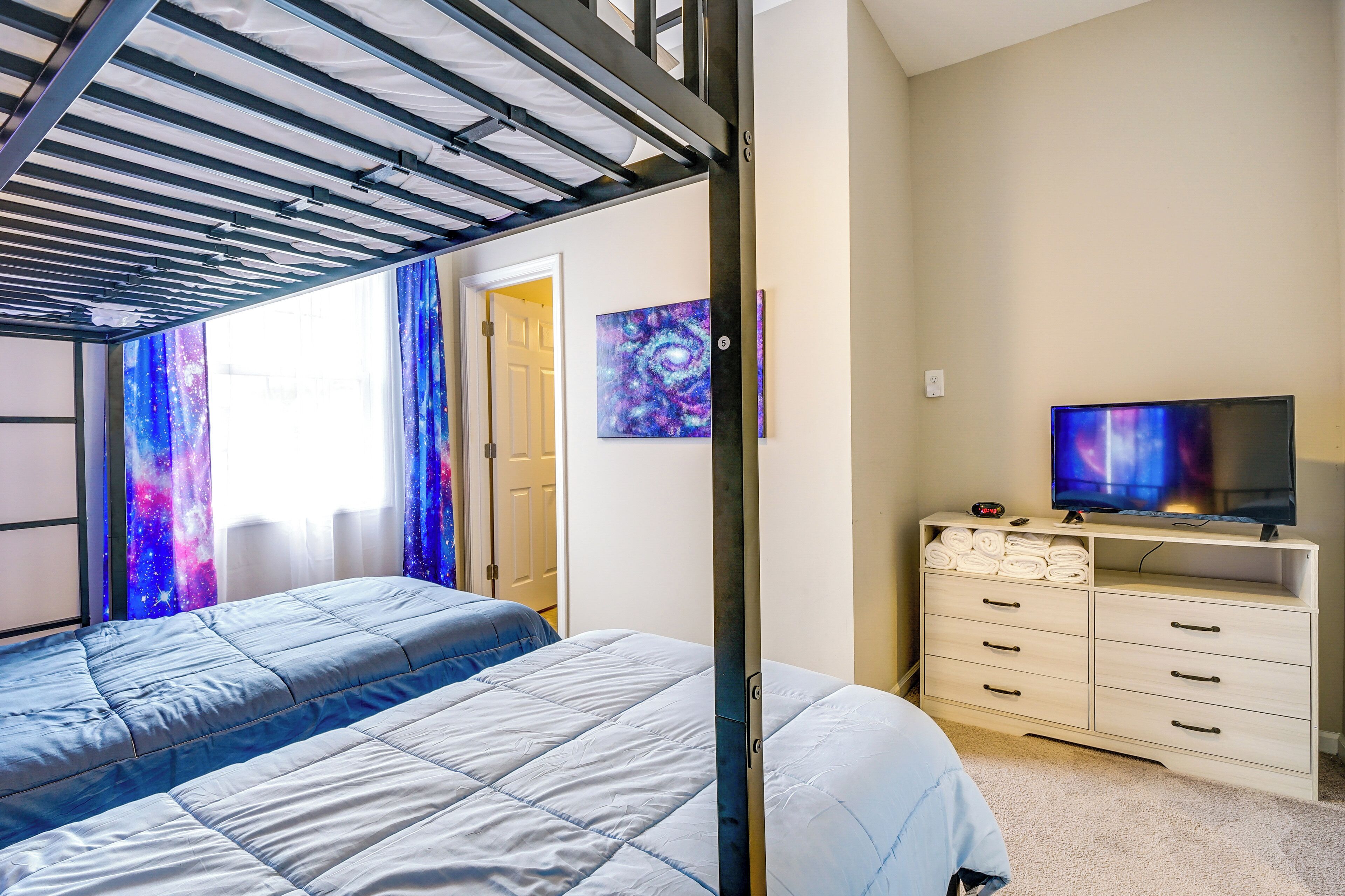 A bedroom with a bunk bed, a TV on a dresser, and a galaxy-themed painting.