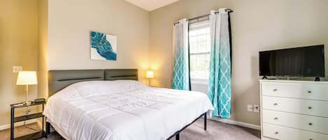 Habitación de hotel con cama, mesita de noche, lámpara, televisión y ventana con cortinas.