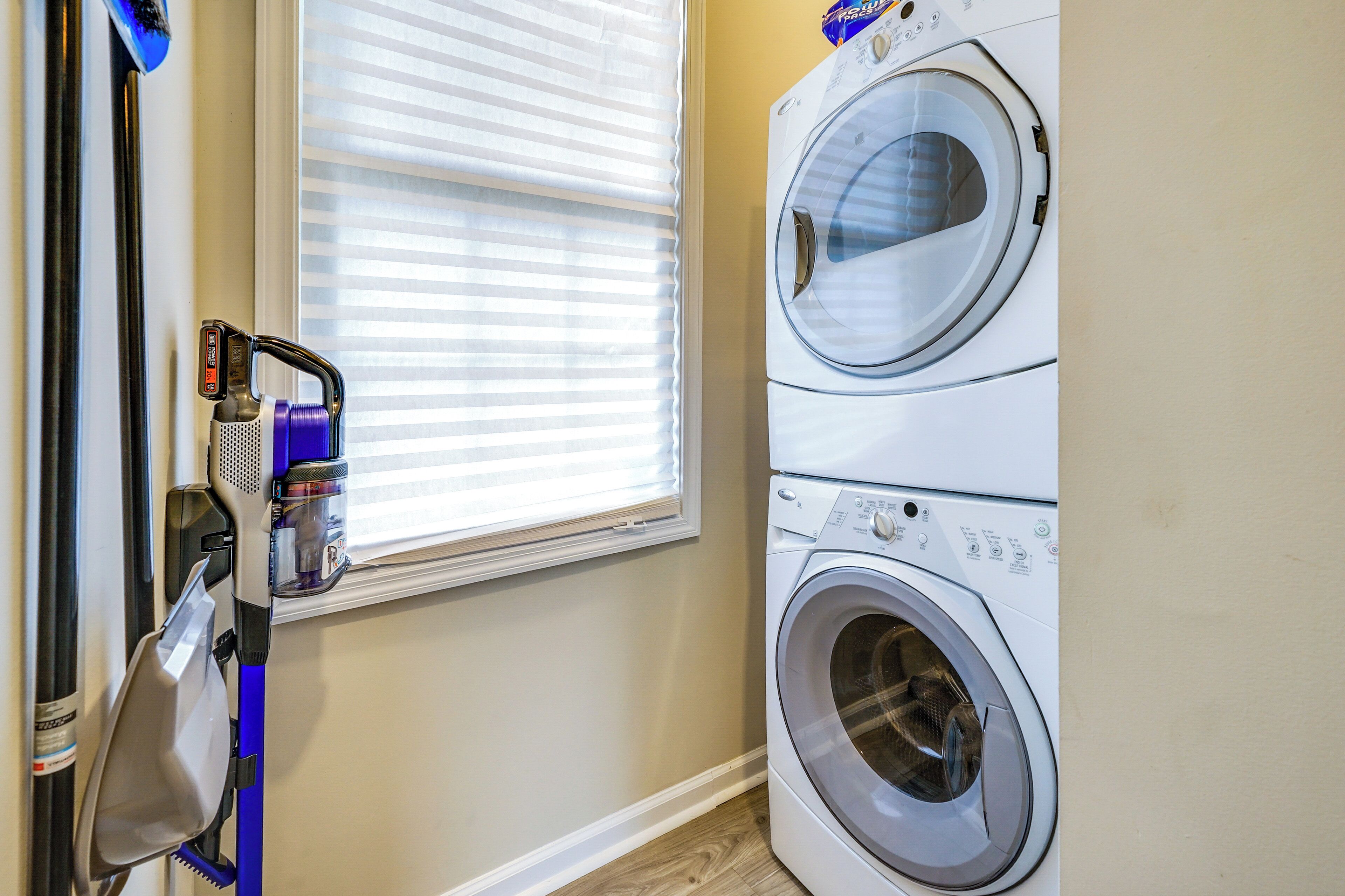 A laundry area with a washing machine and dryer, a window with blinds, and a blue cleaning tool.