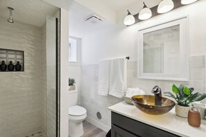 Une salle de bain moderne avec un mur en briques blanches, un grand miroir, un lavabo sur colonne et un espace douche.