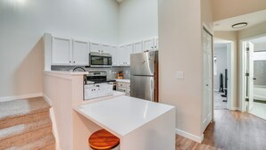 Una cocina moderna con armarios blancos, electrodomésticos de acero inoxidable y un taburete de madera.