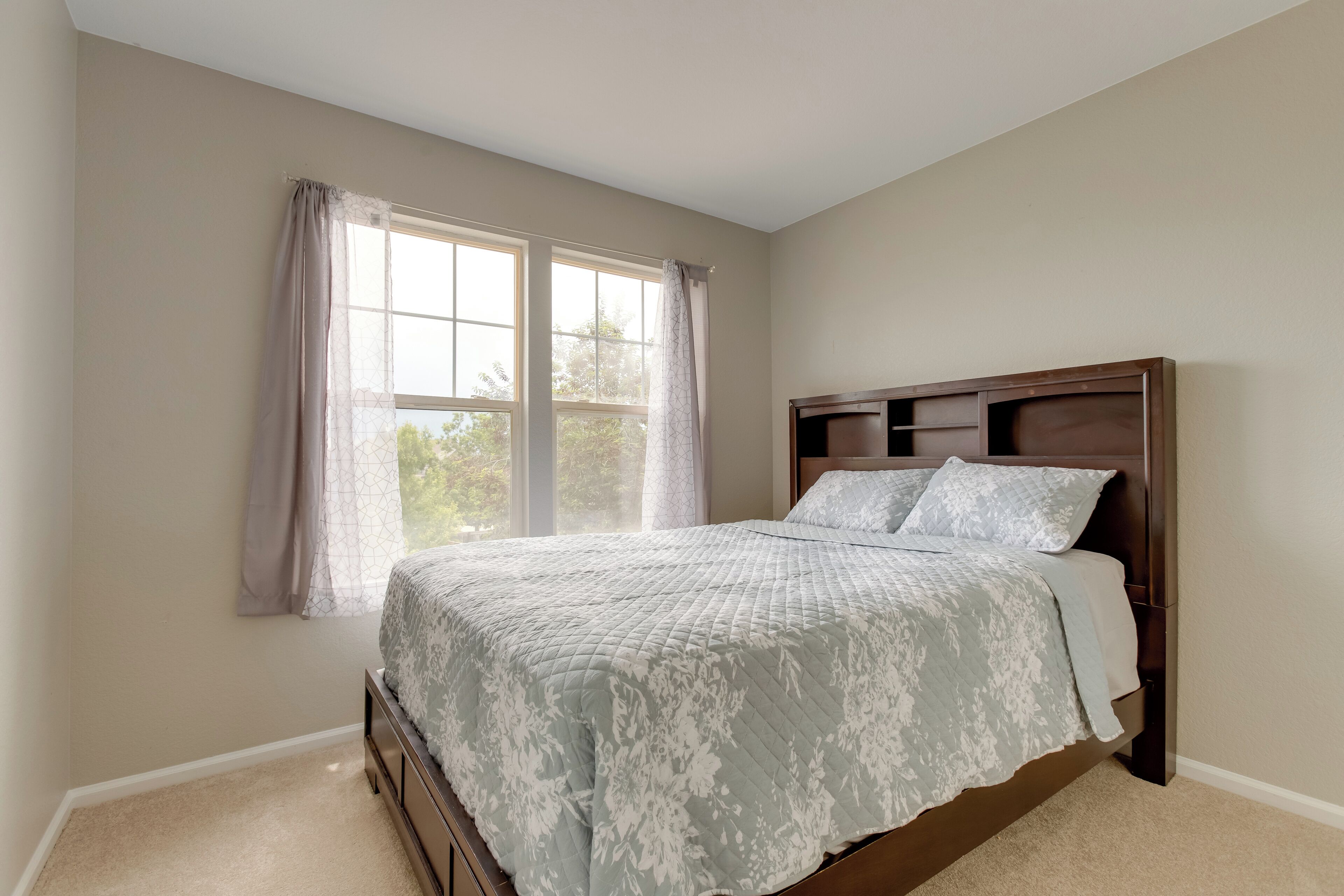 A bedroom with a bed, a window with curtains, and a headboard.