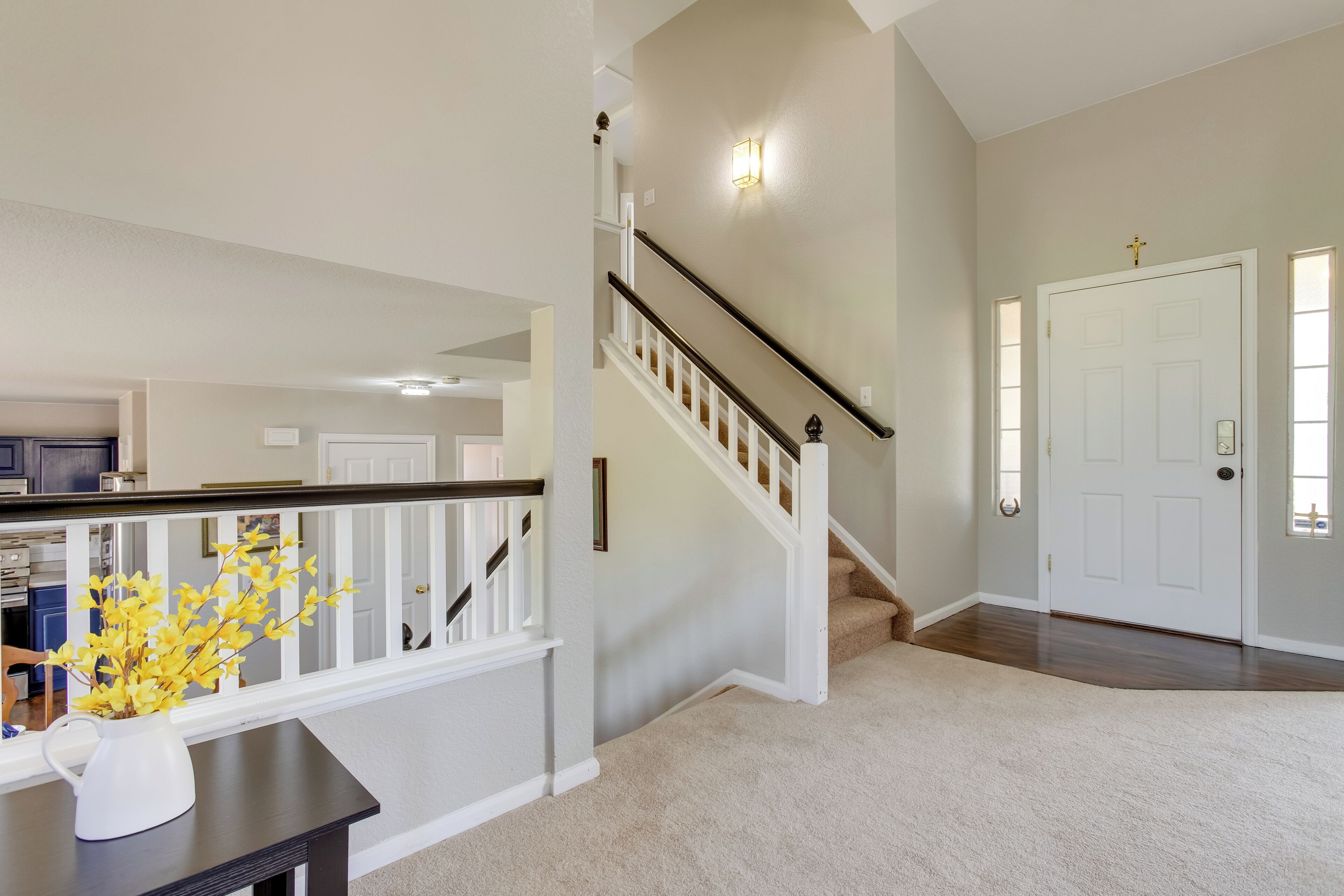 A spacious living area with a staircase, a white door, and a vase of yellow flowers on a table.