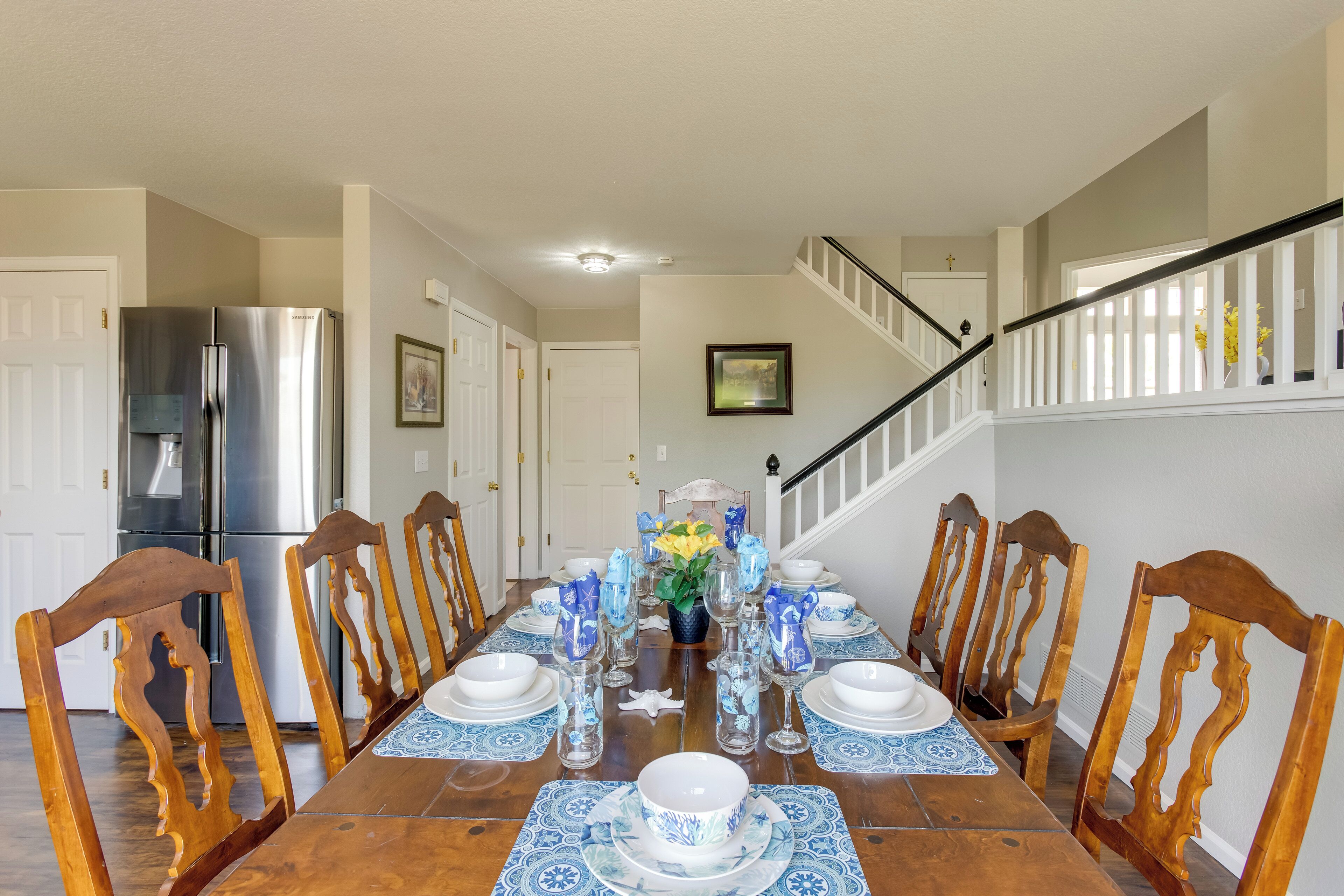 A dining room with a wooden table set for six, surrounded by wooden chairs.