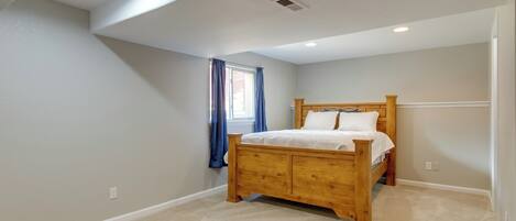 A bedroom with a wooden bed, a window with blue curtains, and a sloped ceiling with recessed lighting.