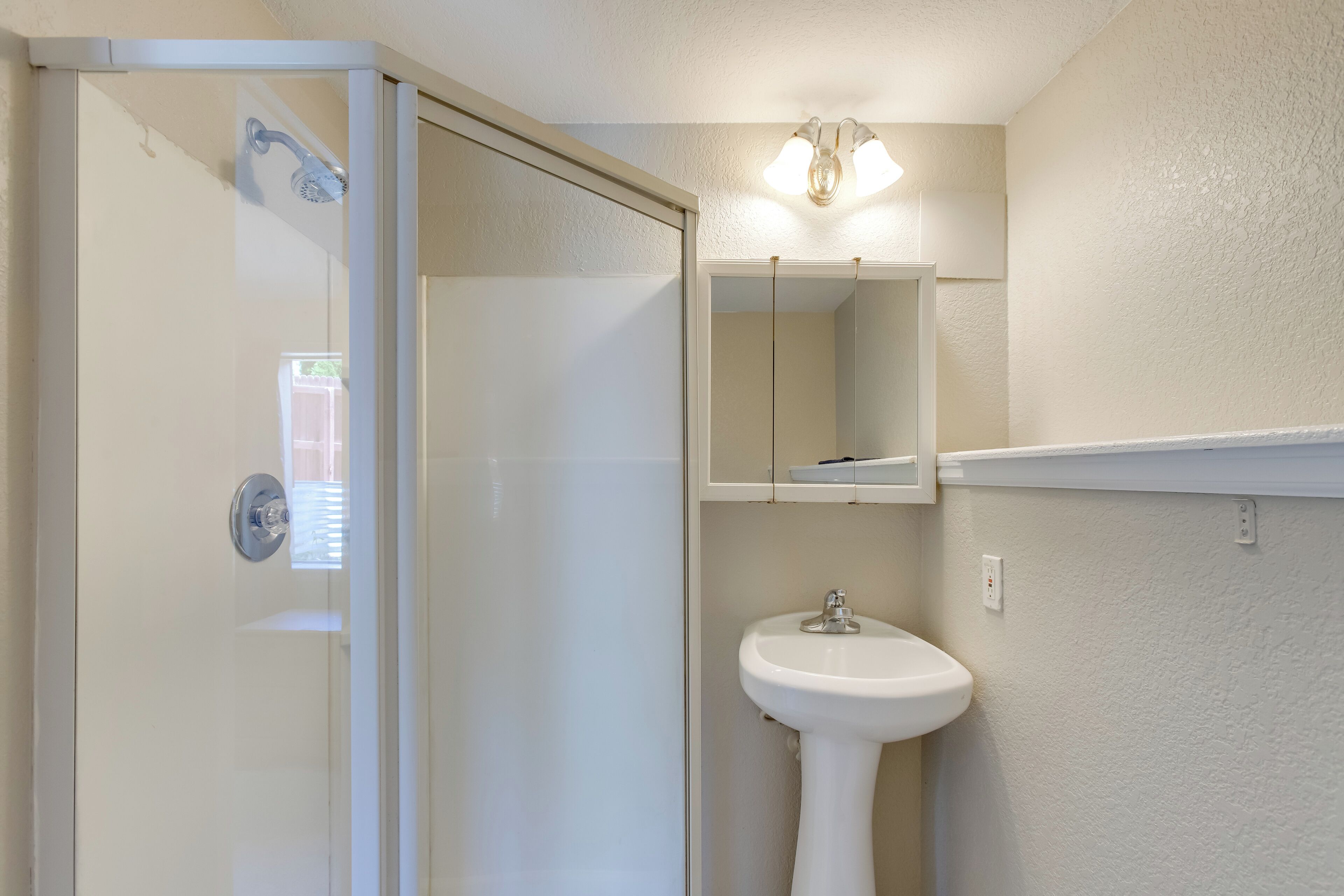 Une salle de bain avec une porte de douche en verre, un lavabo sur colonne et un miroir au-dessus du lavabo.