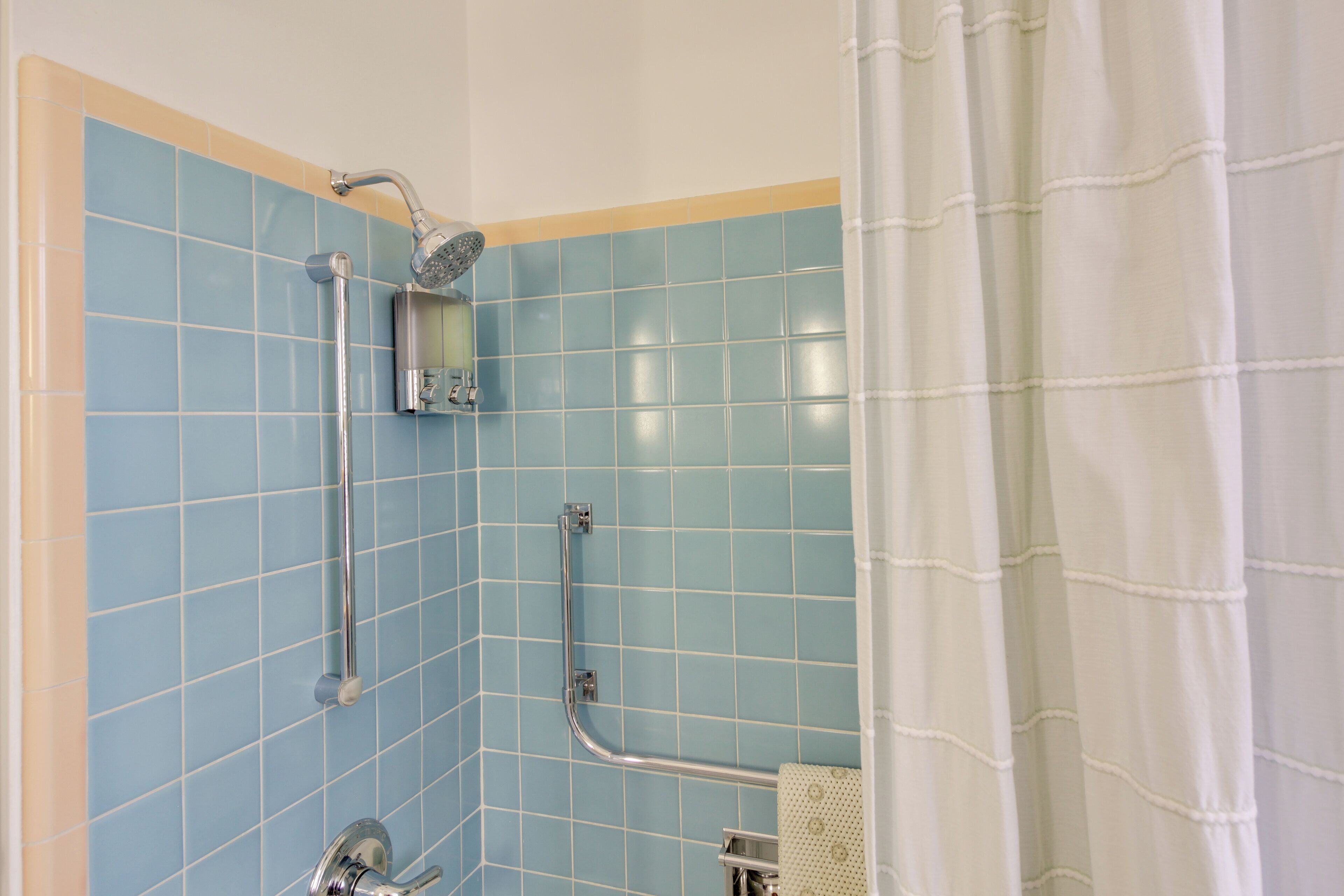 A bathroom with blue tiles, a shower, a grab bar, and a towel rack.