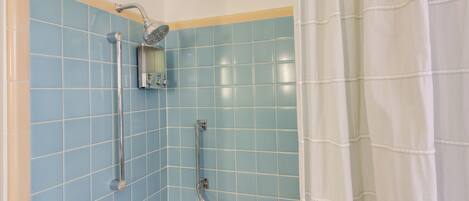 A bathroom with blue tiles, a shower, a grab bar, and a towel rack.