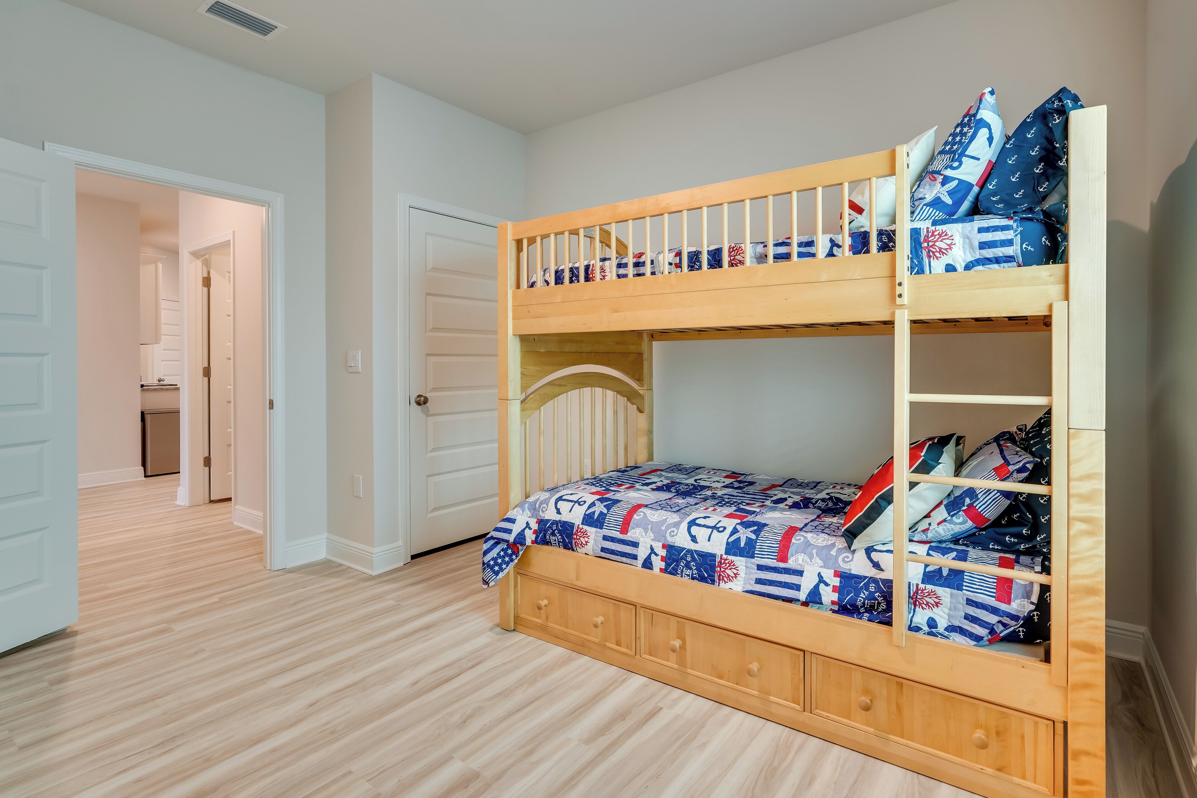 A bunk bed with a storage drawer, a door leading to another room, and a light-colored wooden floor.