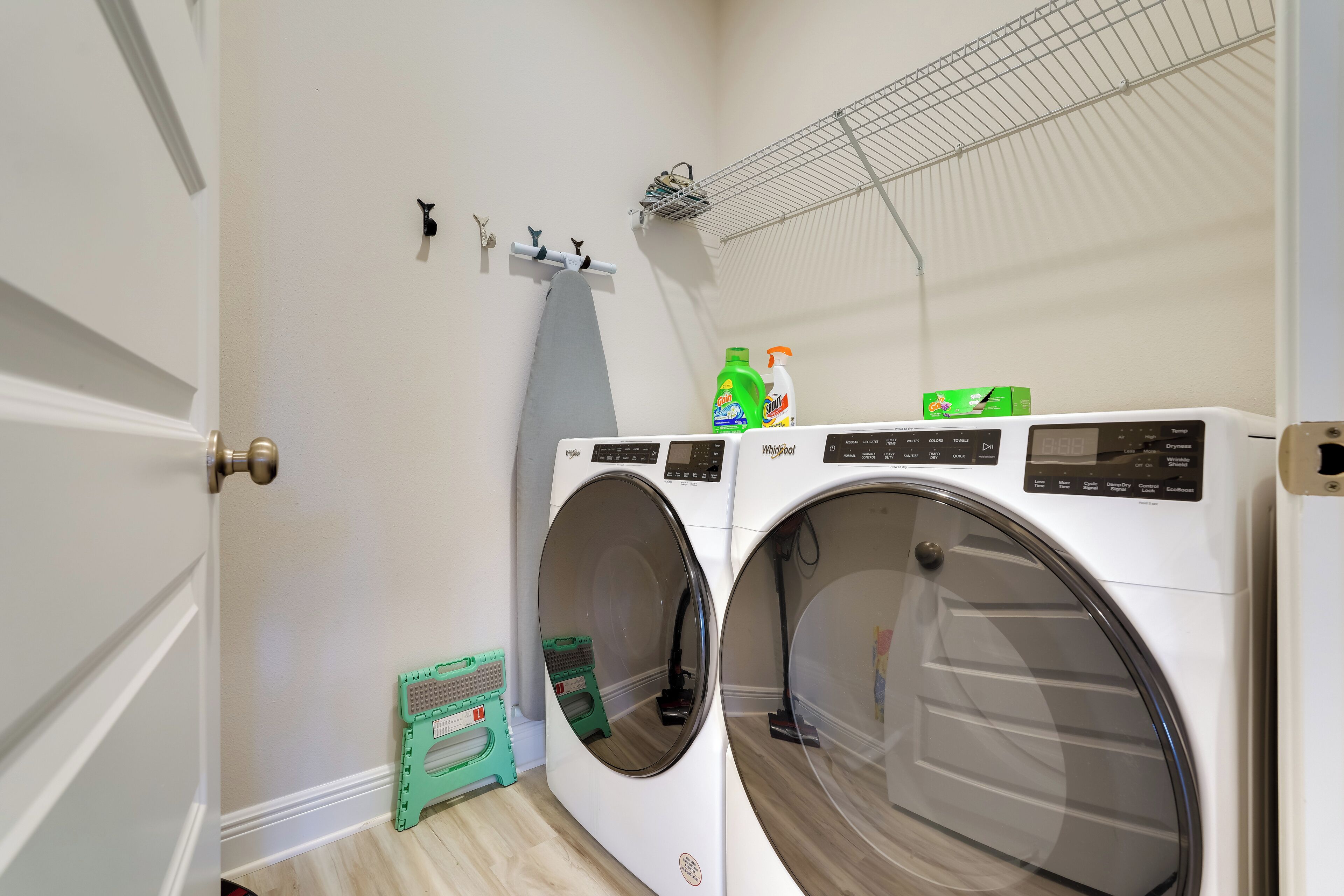 A laundry area with two front-loading washing machines, a drying rack, and a small green step stool.