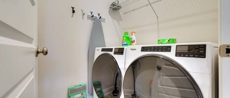 A laundry area with two front-loading washing machines, a drying rack, and a small green step stool.