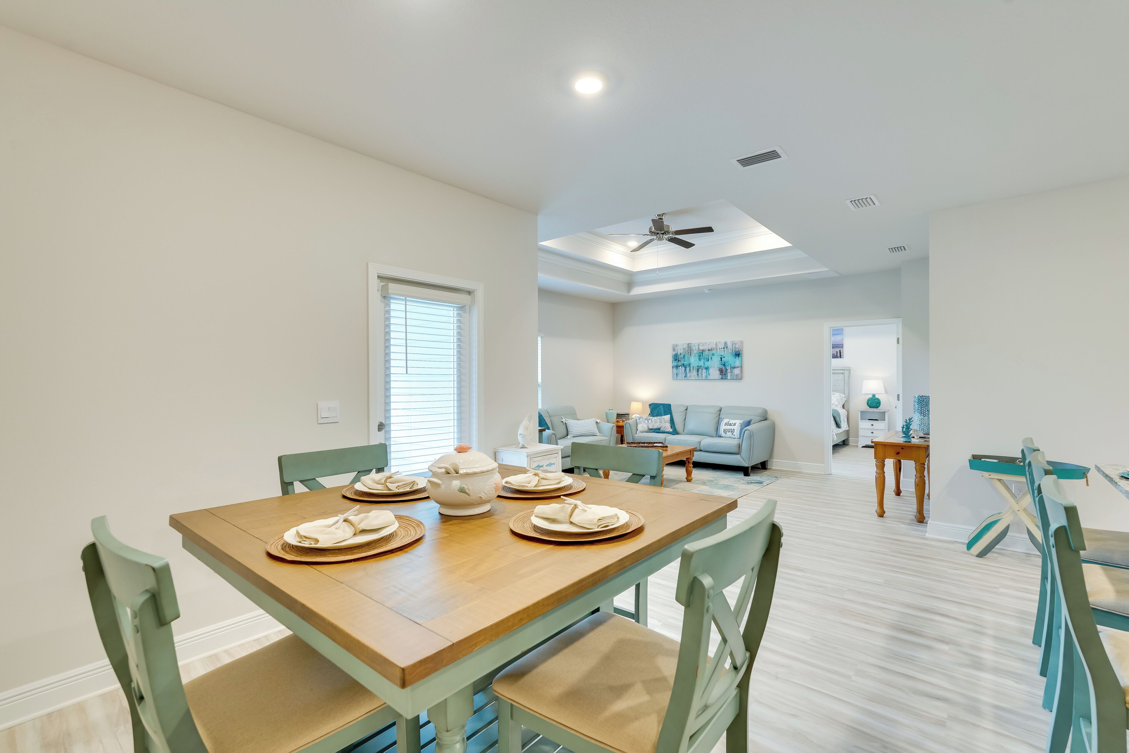 A dining area with a wooden table set for four, green chairs, and a view into a living room with a sofa and a coffee table.