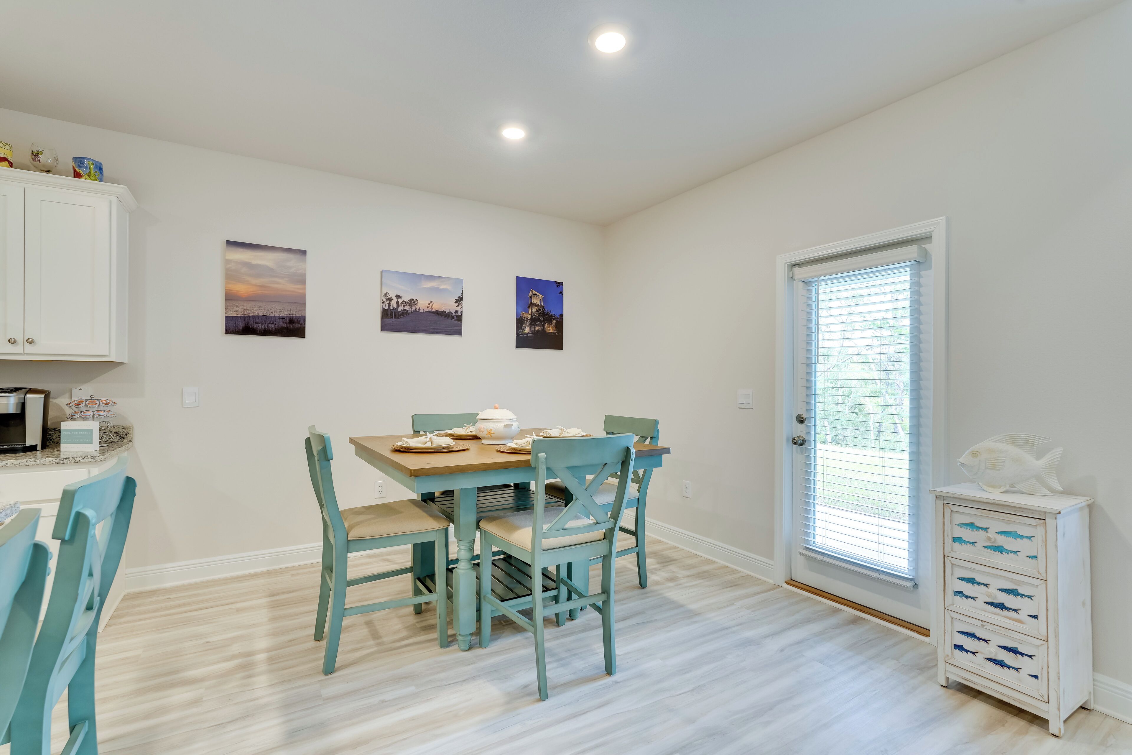 Un coin repas avec une table dressée pour quatre personnes, des chaises de couleur turquoise et un buffet blanc orné d’un motif de poisson.