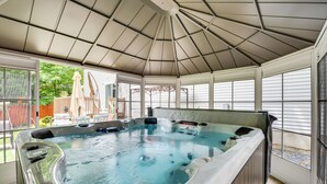 A hot tub under a covered patio with a view of a house and greenery outside. - Hot Tub, Game Room & Fire Pit: Pocono Summit Home! (Pocono Summit)
