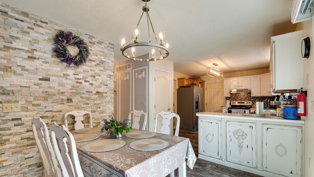 A dining area with a table set for four, surrounded by white chairs, a chandelier, and a decorative wreath on the wall. - Hot Tub, Game Room & Fire Pit: Pocono Summit Home! (Pocono Summit)