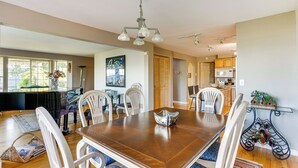 A dining area with a large wooden table, white chairs, and a chandelier. - Federal Way Vacation Rental: Bay & Mountain Views! (Federal Way)