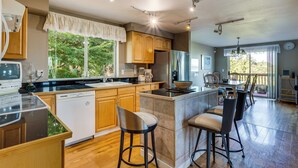 A modern kitchen with wooden cabinets, a dishwasher, and a large island with bar stools. - Federal Way Vacation Rental: Bay & Mountain Views! (Federal Way)