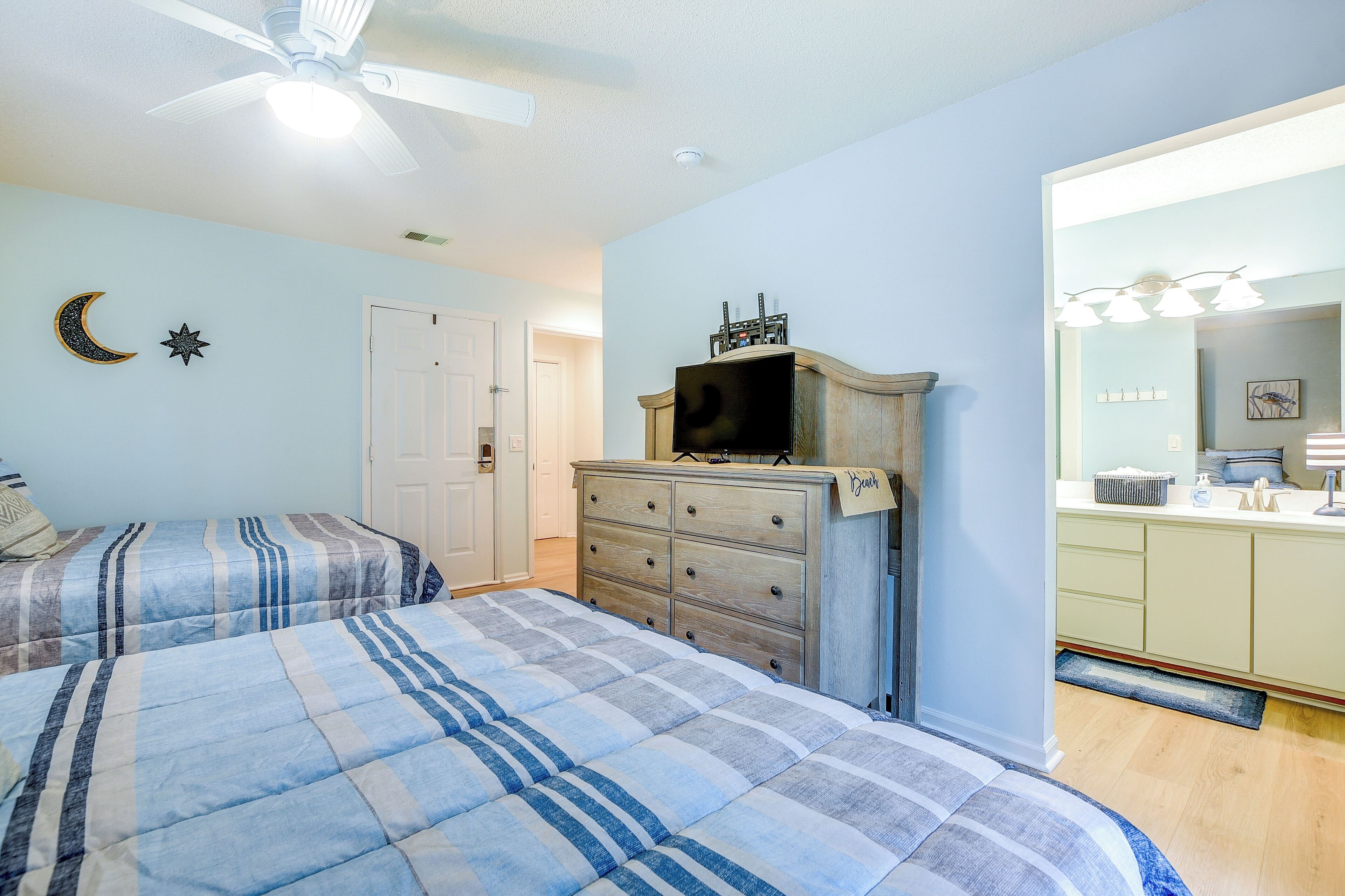 A bedroom with two beds, a dresser, a television on top, and a bathroom with a sink and mirror.