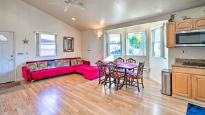 A spacious living room with a bright ceiling fan, a red sectional sofa, a dining area with wooden chairs, and a kitchen with wooden cabinets and a microwave. - San Bruno Vacation Rental - Walk Downtown! (San Bruno)