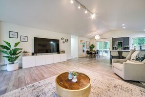 A modern living room with a large flat-screen TV, a round coffee table, and a sofa. There is a dining area with a table and chairs visible in the background. - Issaquah Retreat Near Lake Sammamish State Park! (Issaquah)
