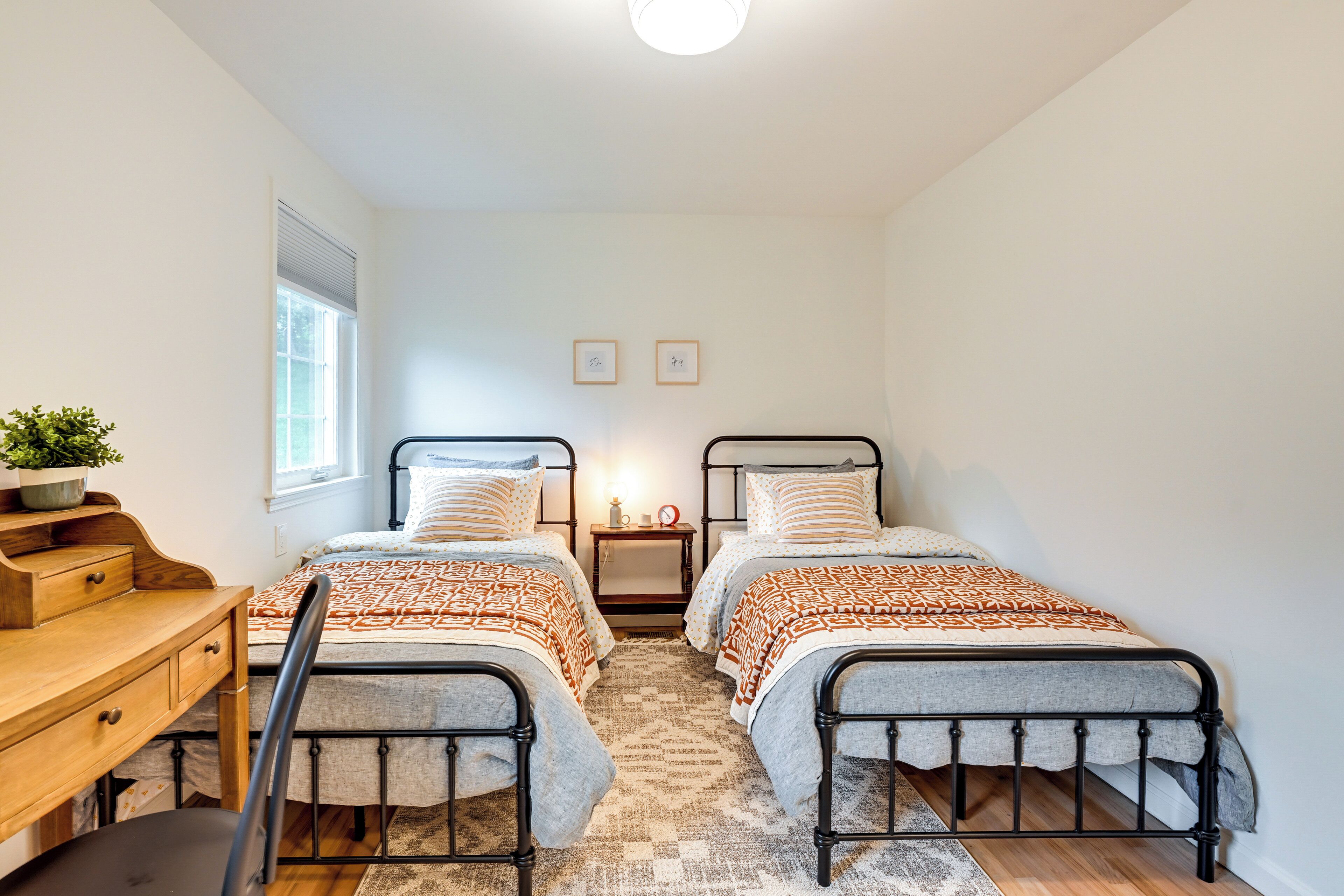 A bedroom with two single beds, a wooden desk, a chair, a nightstand, and a small potted plant.