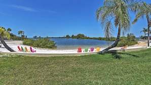 A beach with colorful Adirondack chairs lined up on the sand, a palm tree, and a calm lake in the background. - Tropical Retreat w/ Pool & Tennis Courts in Hudson (Hudson)