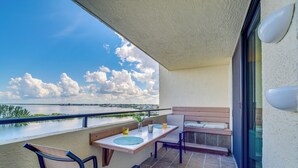 A balcony with a table and chairs, a bench, and a view of a body of water and clouds. - Tropical Retreat w/ Pool & Tennis Courts in Hudson (Hudson)