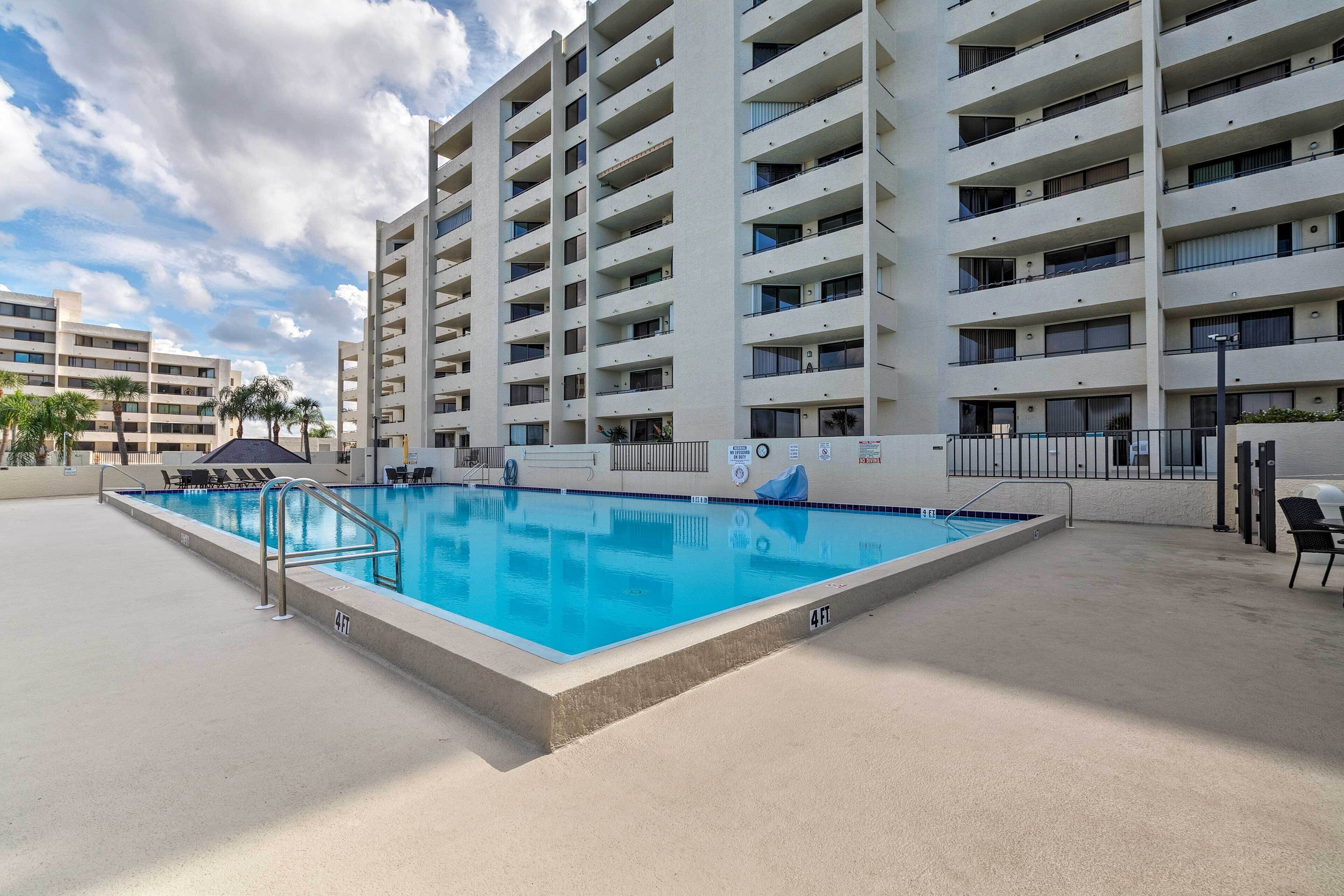 A swimming pool with a 4ft depth marker, surrounded by a concrete deck and a multi-story building with balconies.