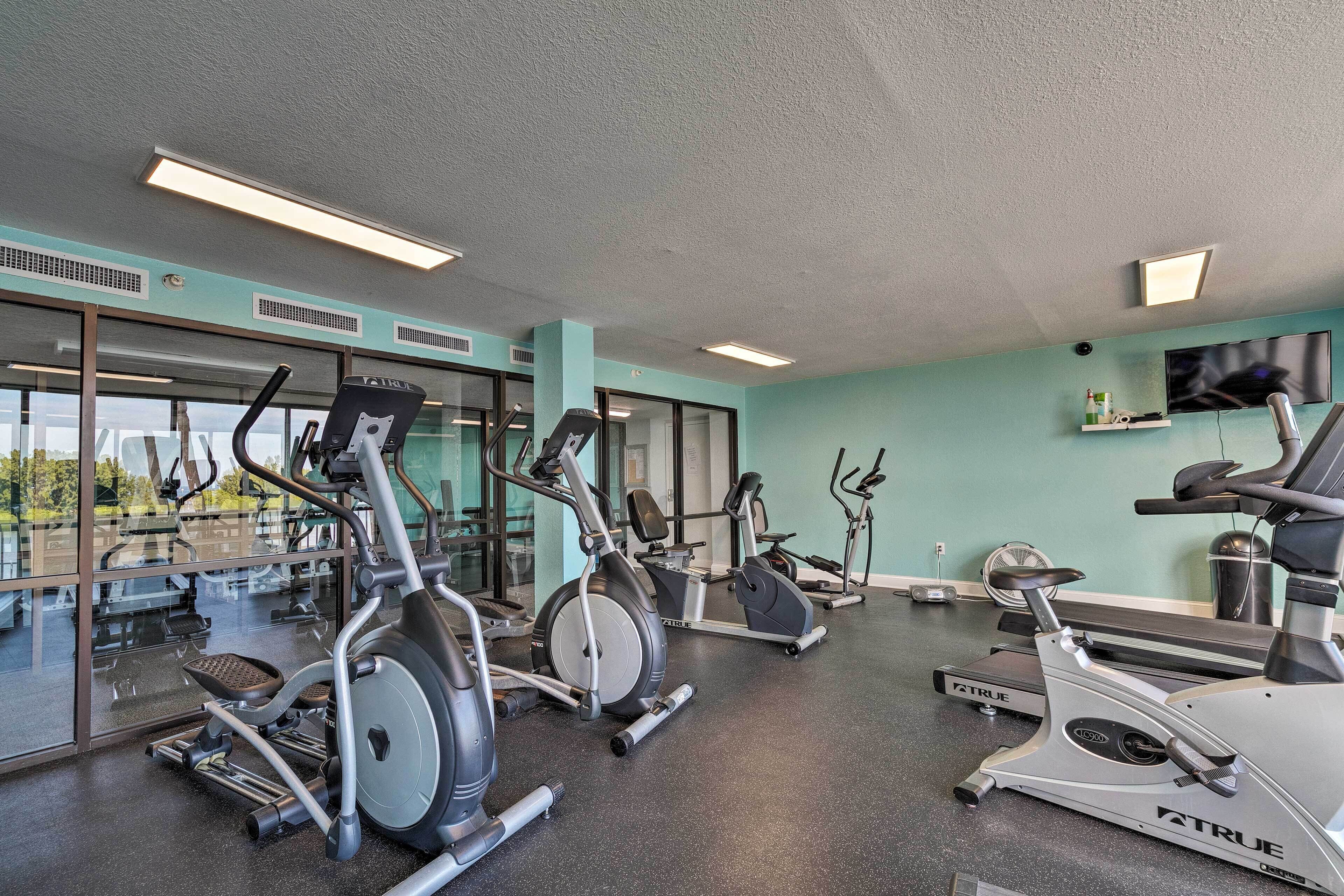 A gym with various exercise machines, large windows, and a teal wall.