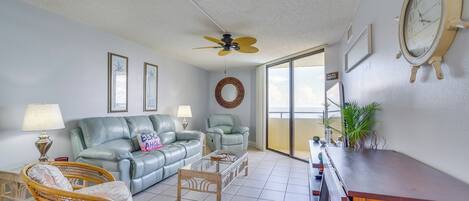 A living room with a sofa, chairs, a coffee table, a ceiling fan, and a dining table.
