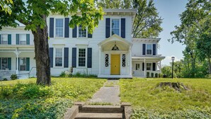 A two-story white house with a yellow front door, a covered porch, and a stone pathway leading to the entrance. - Coxsackie Home w/ River Views: Walk to The Wire! (Coxsackie)