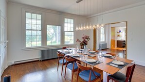 A dining room with a wooden table set for six, large windows, and a view of the outdoors. - Coxsackie Home w/ River Views: Walk to The Wire! (Coxsackie)