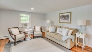 A living room with a beige sofa, two armchairs, a small white side table with a lamp, and a framed picture on the wall. - Middletown Vacation Rental: 2 Mi to Beach! (Middletown)