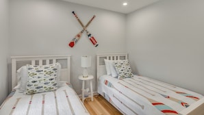 A bedroom with two beds, white bedding, a nightstand with a lamp, and a wall-mounted rack with two bats. - Middletown Vacation Rental: 2 Mi to Beach! (Middletown)