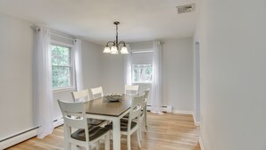 A dining room with a wooden table, white chairs, and a chandelier. - Middletown Vacation Rental: 2 Mi to Beach! (Middletown)