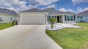 A residential house with a garage, a well-maintained lawn, and a clear sky. - Pool Access: Sleek Home in The Villages w/ Lanai (Wildwood)