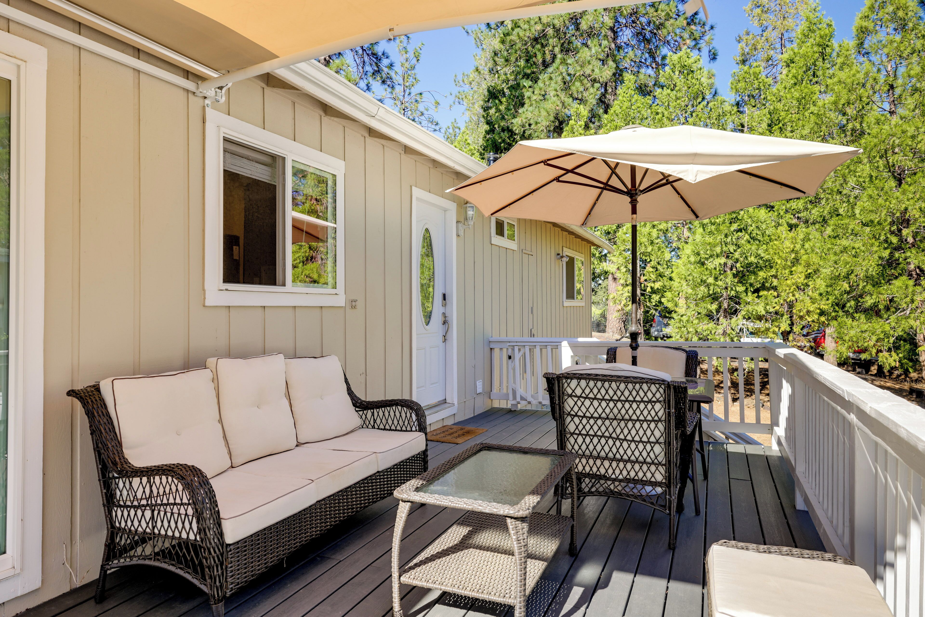A covered deck with a wicker sofa, a glass table, and an umbrella.