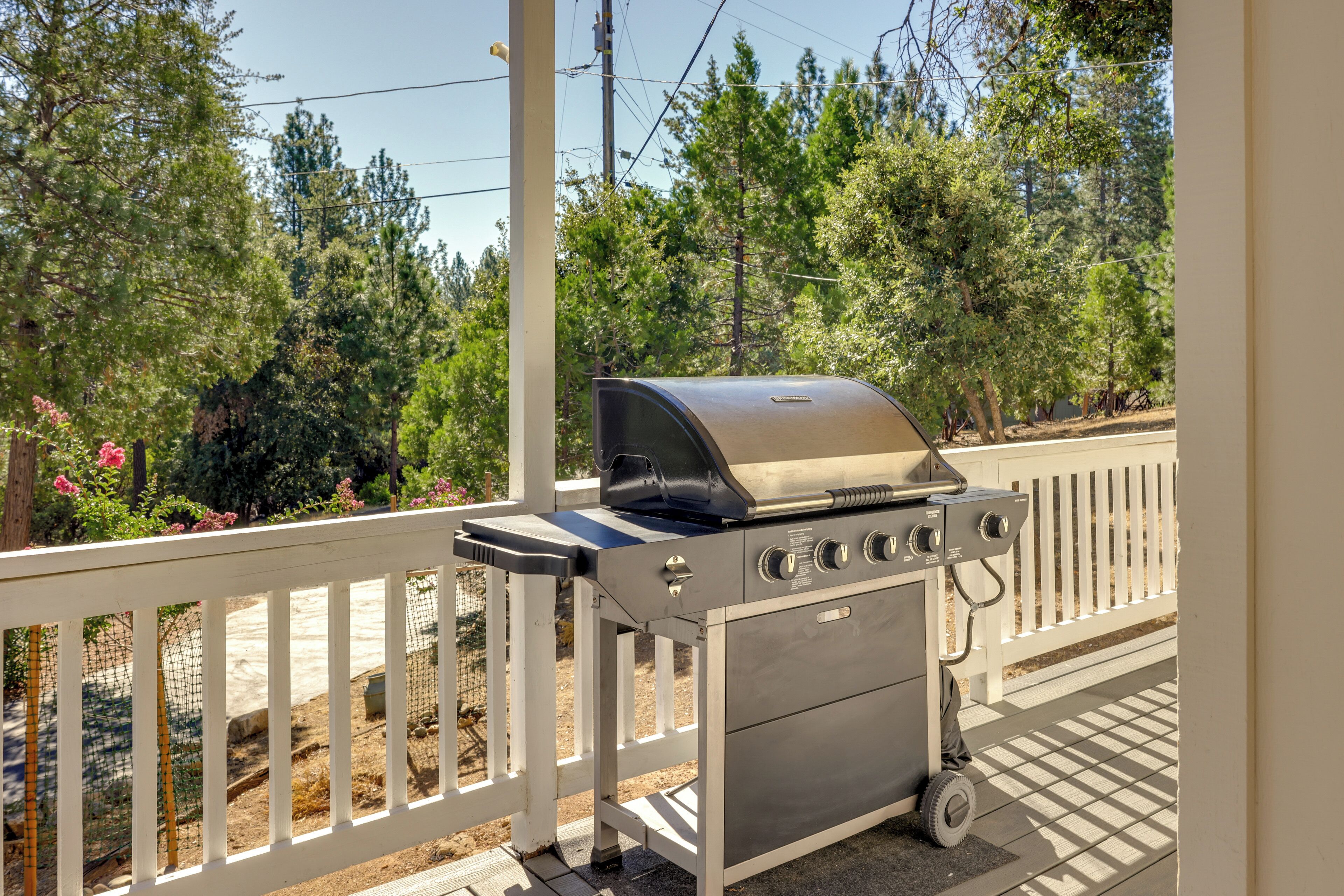 Un barbecue portable sur une véranda dotée d’une balustrade blanche, entouré d’arbres et sous un ciel dégagé.