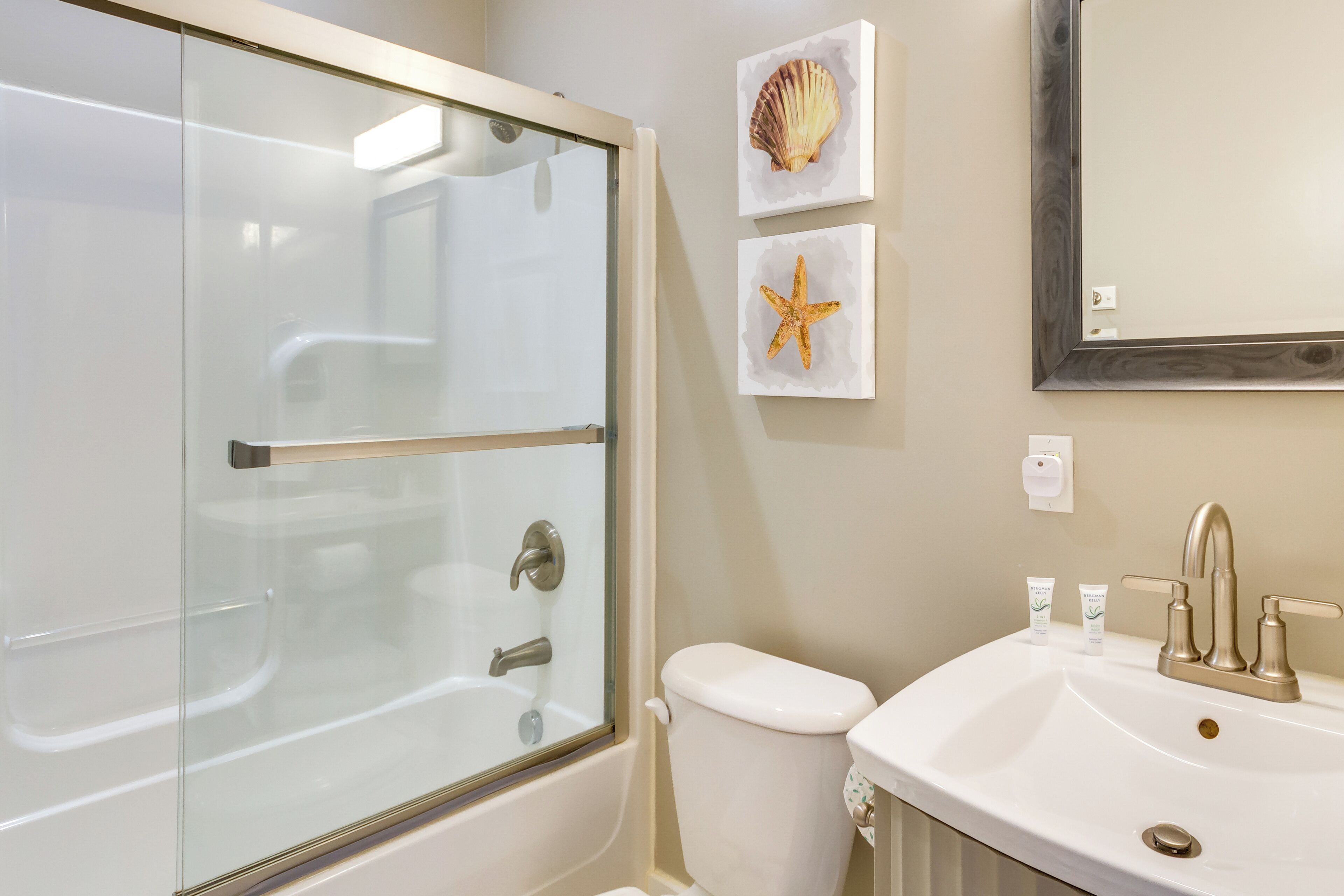 A bathroom with a glass-enclosed shower, a white sink with a single faucet, and two framed pictures on the wall.