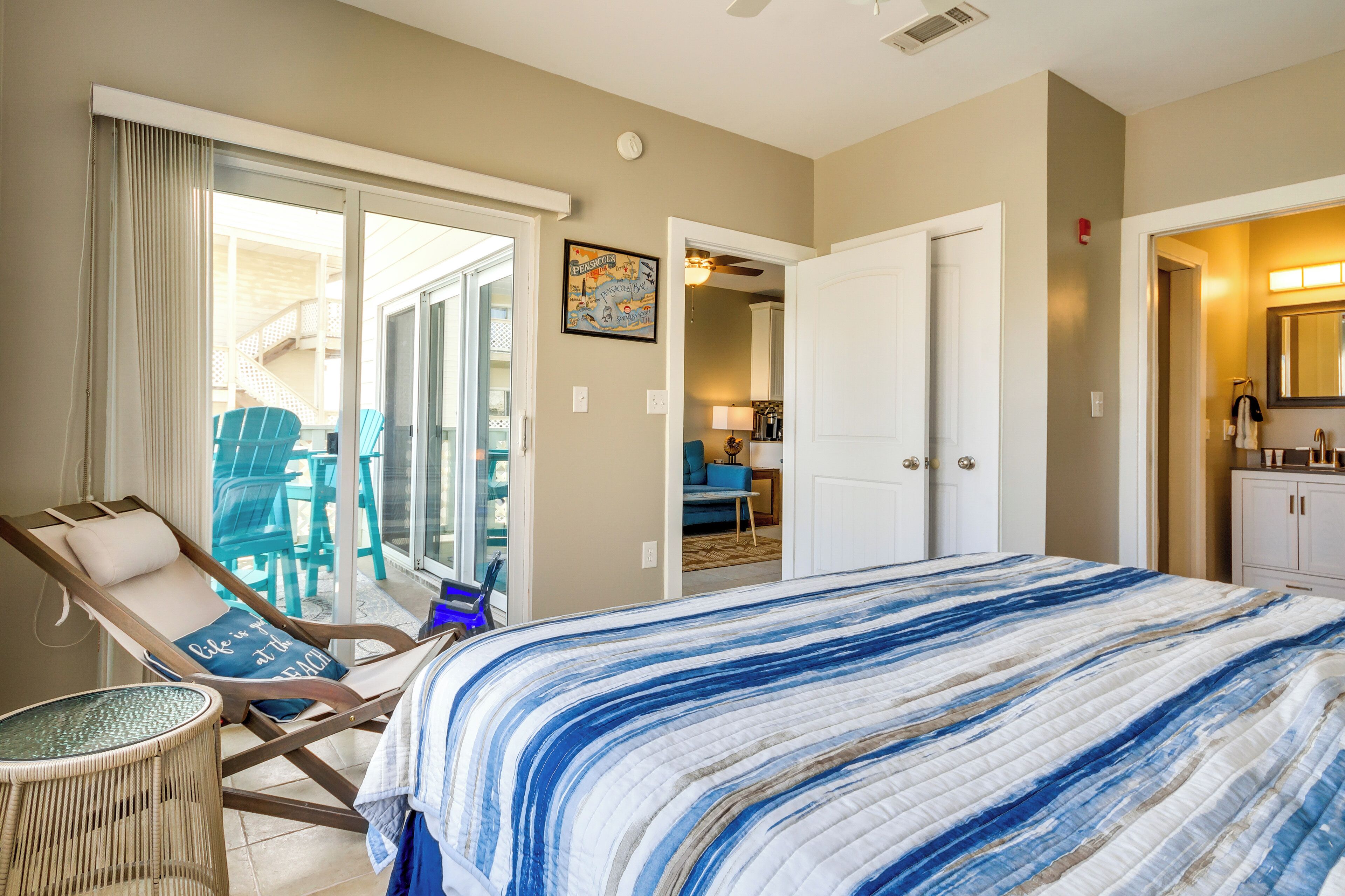 Ein Schlafzimmer mit einem großen Bett, einem Sessel, einem Balkon und einem durch eine geöffnete Tür einsehbaren Badezimmer.