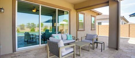 A covered patio with a sliding glass door, a ceiling fan, and outdoor furniture including a sofa and chairs.