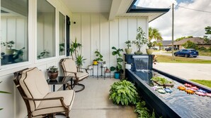 A covered porch with a seating area, potted plants, and a water feature with floating lotus flowers. - Luxe Gulf Breeze Vacation Rental: Furnished Patio! (Gulf Breeze)