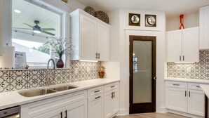 A modern kitchen with white cabinets, a double sink, and decorative wall tiles. - Luxe Gulf Breeze Vacation Rental: Furnished Patio! (Gulf Breeze)
