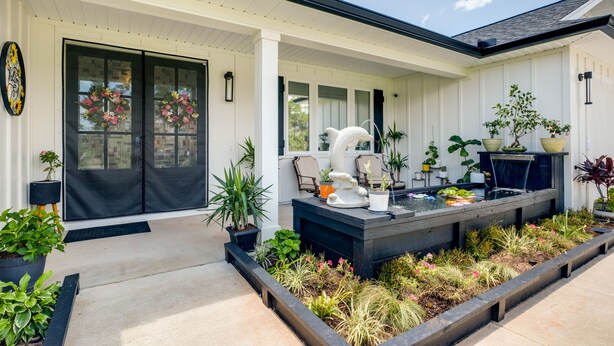 A modern house with a covered porch, a koi pond, and various potted plants. - Luxe Gulf Breeze Vacation Rental: Furnished Patio! (Gulf Breeze)