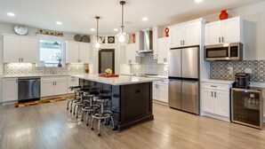 A modern kitchen with white cabinetry, a central island with bar stools, stainless steel appliances, and decorative wall art. - Luxe Gulf Breeze Vacation Rental: Furnished Patio! (Gulf Breeze)